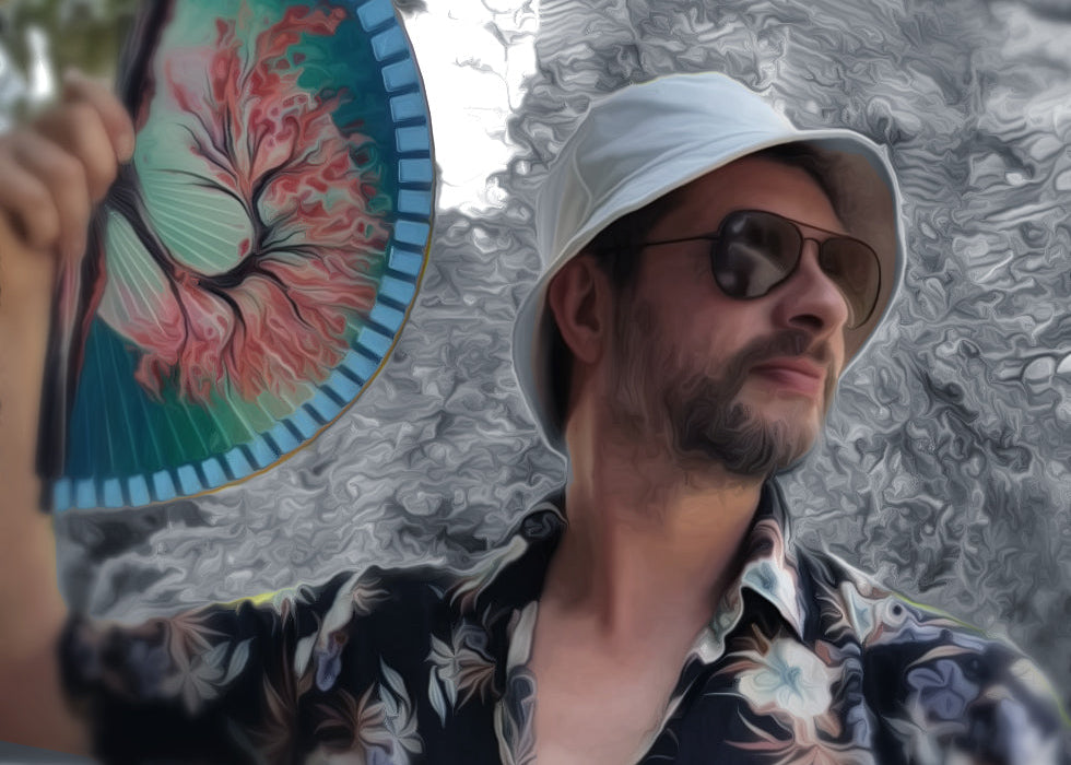 Man wearing a white hat and sunglasses, holding a colorful fan with a tree design.
